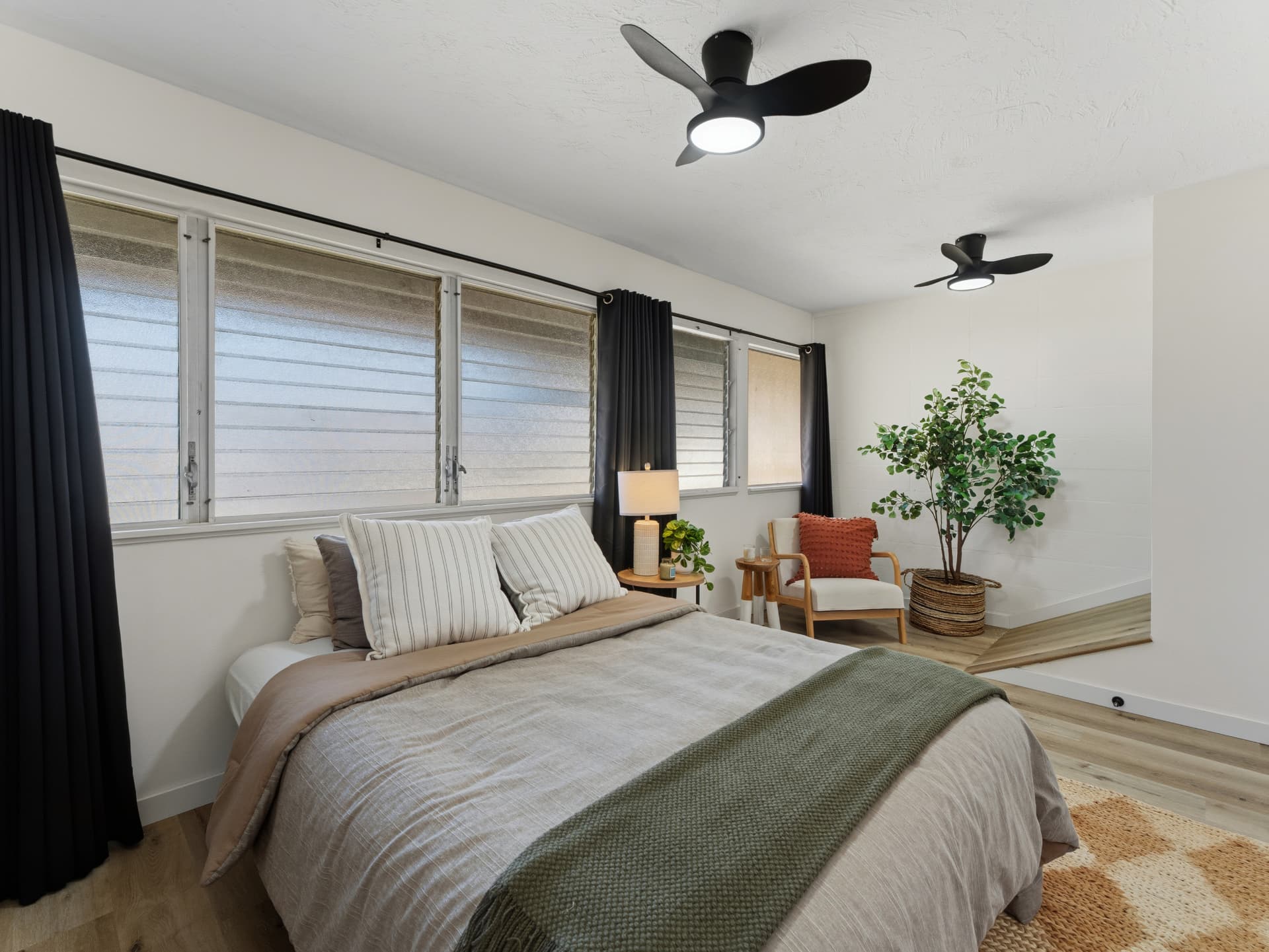 Bedroom with jalousie windows framed by dark curtains and black ceiling fans