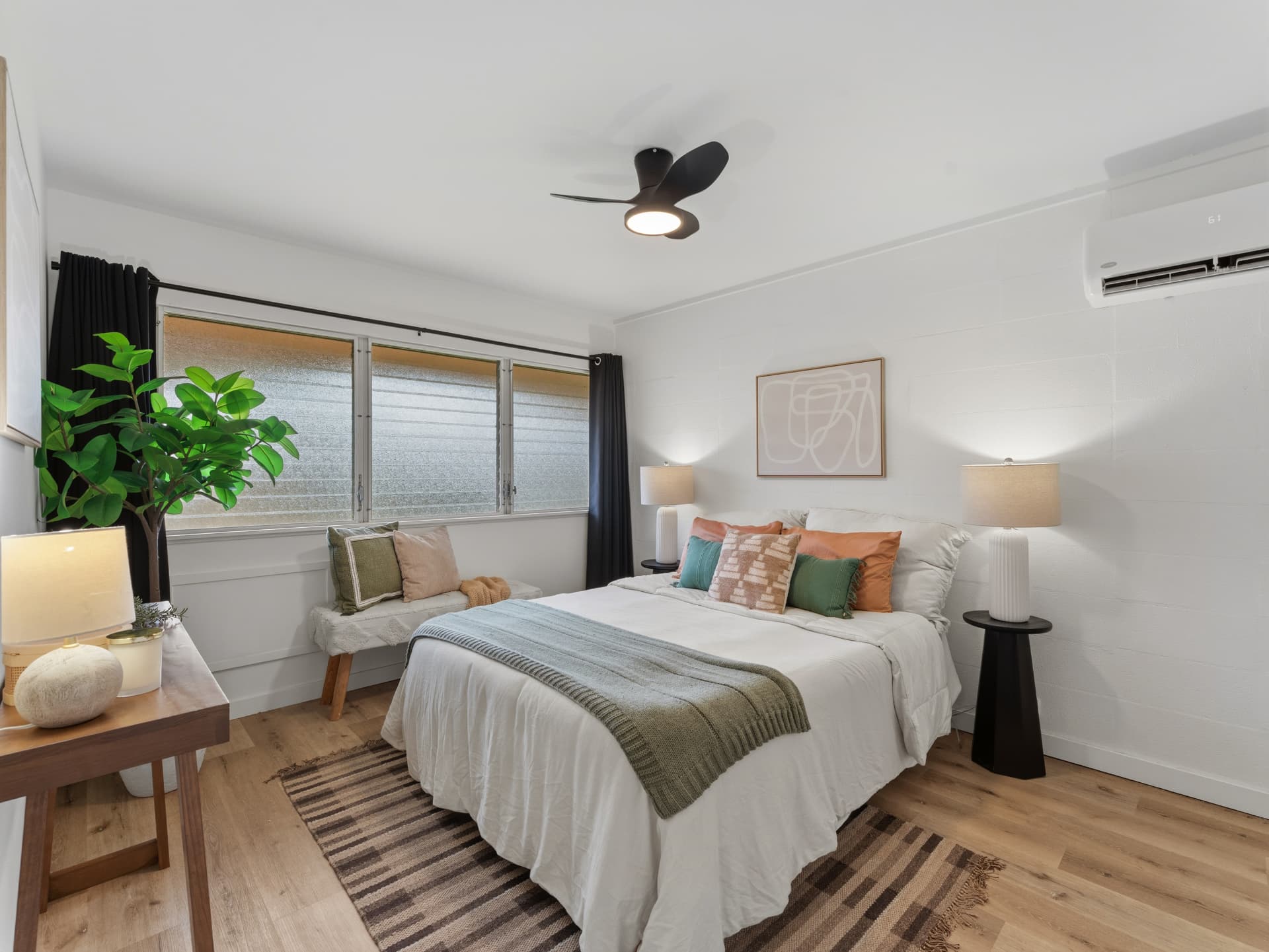 Bright bedroom with a dressed bed, striped rug and a cushioned window bench